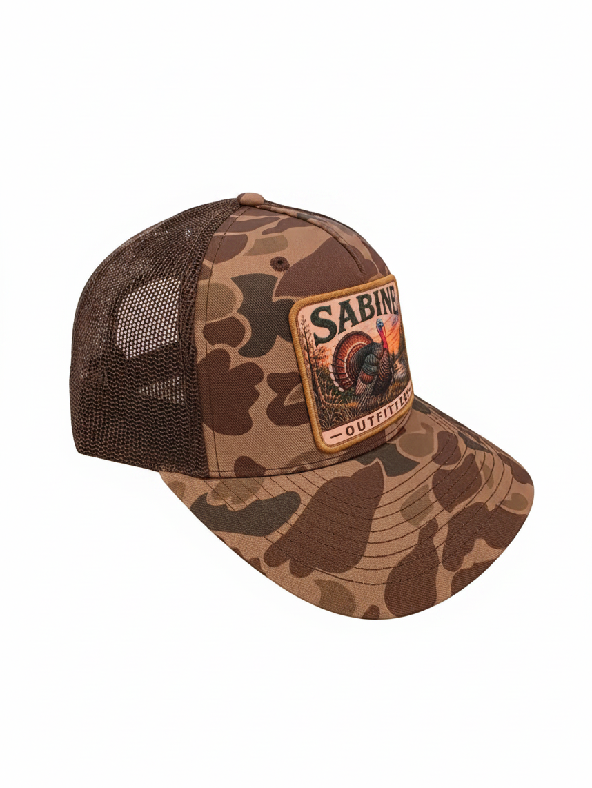 Sabine Outfitters camo trucker hat with a turkey patch and brown mesh back, featuring an adjustable snapback closure.