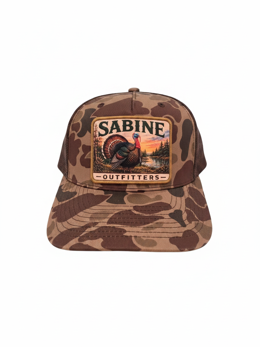 Sabine Outfitters camo trucker hat with a turkey patch, brown mesh back, and adjustable snapback closure.